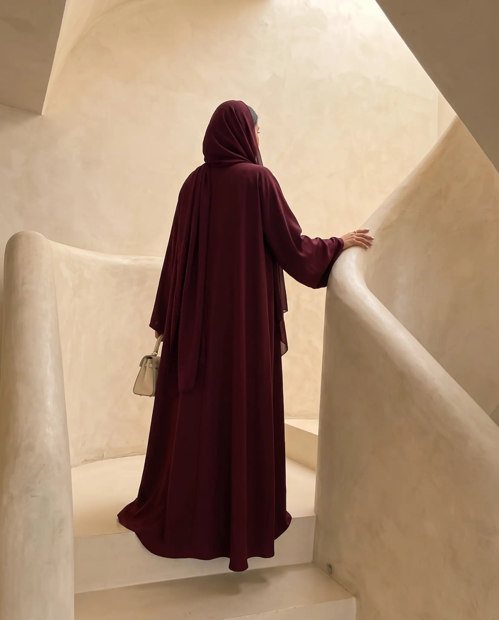 A flowing Velour abaya against sunlit beige architectural curves